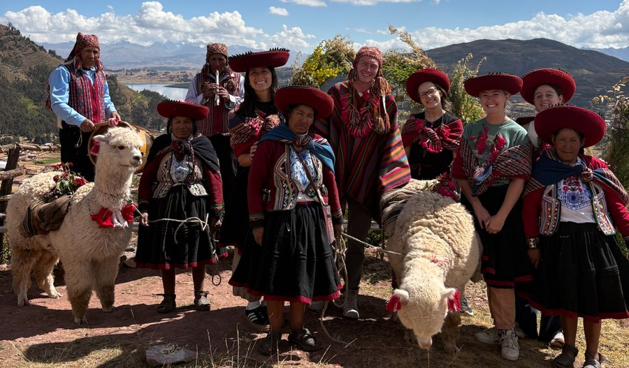 Group in traditional Quechua dress with a llama and sheep, overlooking the Sacred Valley near Cusco, Peru